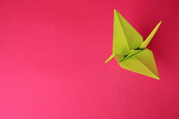 Origami art. Handmade paper crane on pink background, above view. Space for text