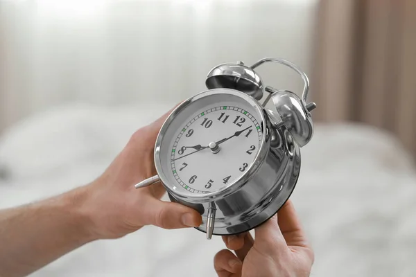 Man with alarm clock in bedroom, closeup of hands