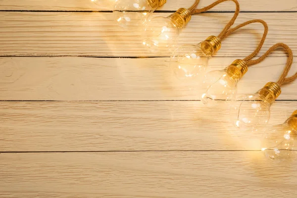 String lights with lamp bulbs on wooden background, top view. Space for text