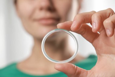 Woman holding diaphragm vaginal contraceptive ring on blurred background, closeup