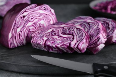 Slices of fresh ripe red cabbage and knife on grey table, closeup