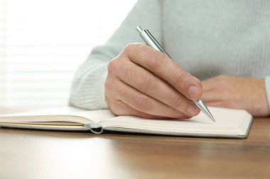 Man writing in notebook at wooden table, closeup