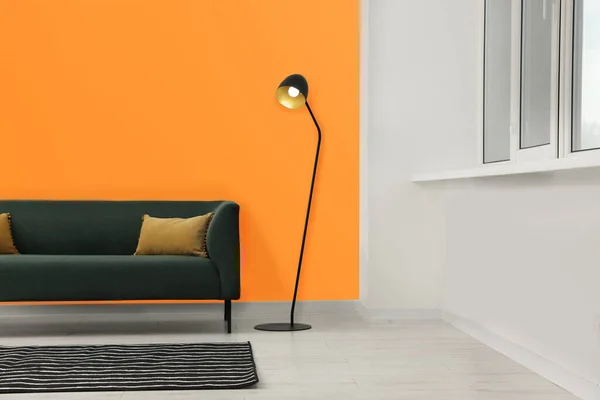 Beautiful interior with sofa and floor lamp near orange wall