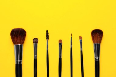 Sarı arka planda makyaj fırçaları, düz yatış. Metin için boşluk