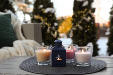 Beautiful burning candles and lantern on table outdoors. Cozy winter