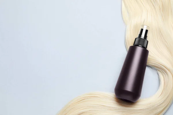 Spray bottle with thermal protection and lock of blonde hair on light background, flat lay. Space for text
