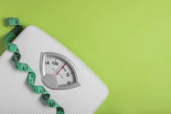 Weight loss concept. Scales and measuring tape on green background, top view. Space for text