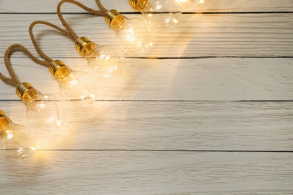 String lights with lamp bulbs on wooden background, top view. Space for text