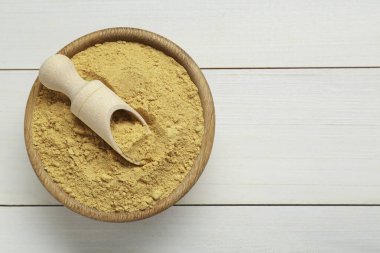 Bowl and scoop with aromatic mustard powder on white wooden table, top view. Space for text
