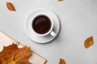 Cup of hot drink, book and autumn leaves on light grey textured table, flat lay