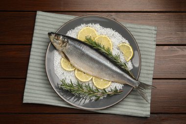 Delicious salted herring, rosemary, salt and lemon on wooden table, top view