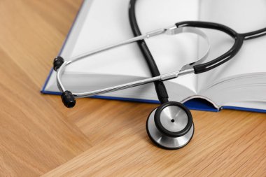 Book and stethoscope on wooden table, closeup