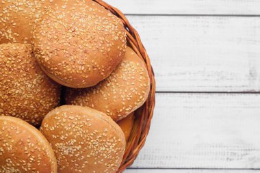 Wicker basket of fresh buns with sesame seeds on white wooden table, top view. Space for text