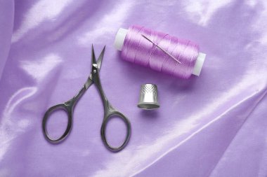 Thimble, scissors and sewing thread on purple cloth, flat lay. Space for text