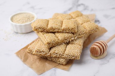 Delicious sweet kozinaki bars, sesame seeds and wooden dipper on white marble table, closeup