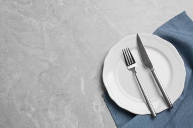Clean plate with shiny silver cutlery on grey marble table, flat lay. Space for text