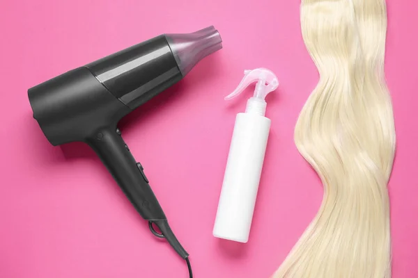 Spray bottle with thermal protection, stylish hairdryer and lock of blonde hair on pink background, flat lay