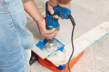 Worker with electric drill preparing tiles for installation indoors, closeup