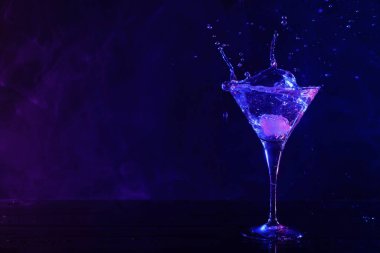Martini splashing out of glass in neon lights, space for text