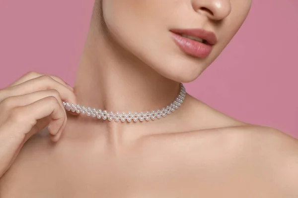 Young woman wearing elegant pearl necklace on pink background, closeup