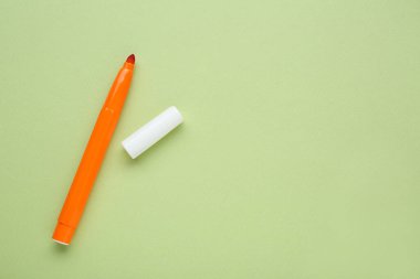 Orange marker with cap on light green background, flat lay. Space for text