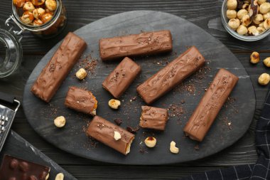Board with delicious chocolate bars, caramel and nuts on black wooden table, flat lay