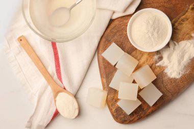 Agar-agar jelly cubes and powder on white marble table, flat lay