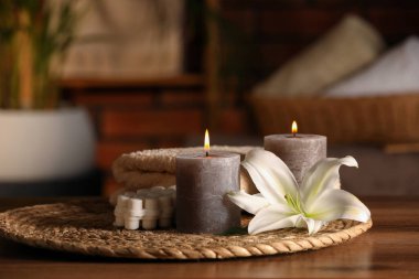 Spa composition with burning candles, lily flower and towels on wooden table in wellness center