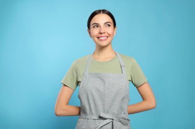 Young woman in grey apron on light blue background,