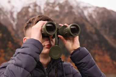 Boy looking through binoculars in beautiful mountains, closeup