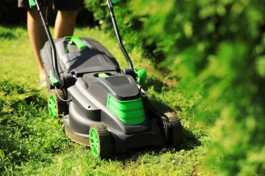 Güneşli bir günde bahçede çim biçme makinesiyle çim biçen adam, yakın plan.