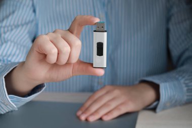 Woman holding usb flash drive at table, closeup