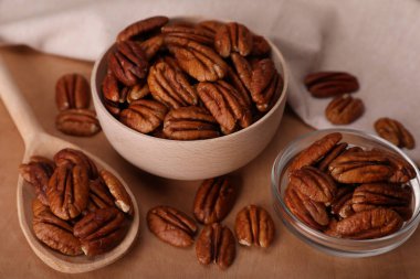Bowls and spoon with tasty pecan nuts on wooden table, closeup