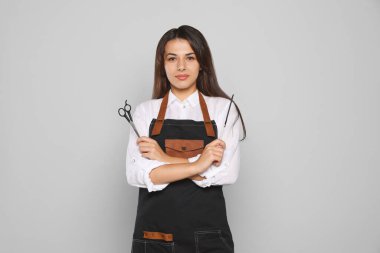 Portrait of happy hairdresser with professional scissors and comb against light grey background