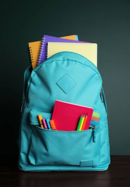 Tahtanın yanındaki beyaz masanın üzerinde farklı okul kırtasiyesi olan sırt çantası.