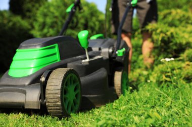 Güneşli bir günde bahçede çim biçme makinesiyle çim biçen adam, yakın plan.