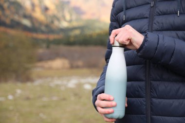 Boy holding thermo bottle in beautiful mountains, closeup. Space for text