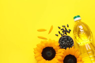 Bir şişe yağ, ayçiçeği ve tohumlar sarı arka planda, düz yerde. Metin için boşluk