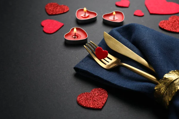 Cutlery set, burning candles and decorative hearts on black background, space for text. Romantic table setting