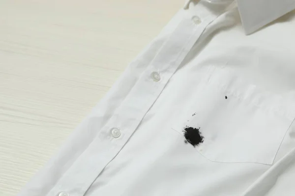 White shirt with stain of black ink on wooden table, closeup. Space for text
