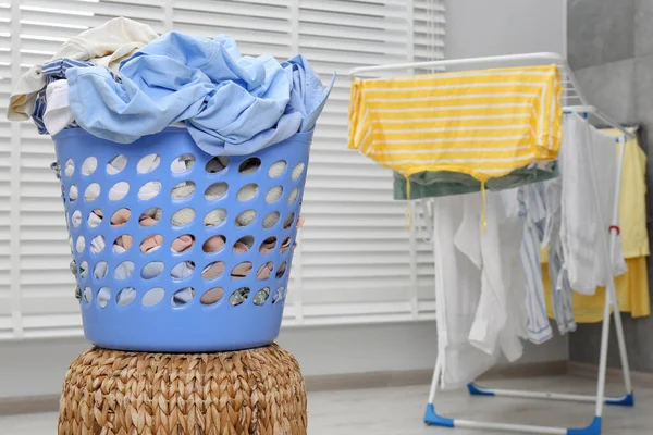 Plastic laundry basket with clothes on wicker pouf indoors. Space for text