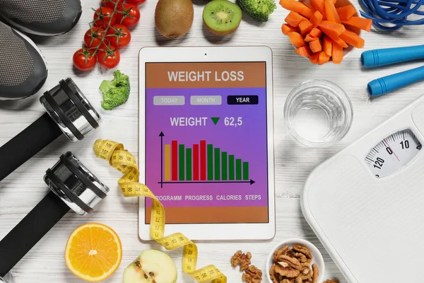 Tablet with weight loss calculator application, fitness items and different products on white wooden table, flat lay
