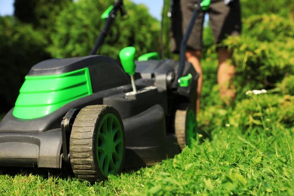 Güneşli bir günde bahçede çim biçme makinesiyle çim biçen adam, yakın plan.