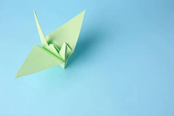 Origami art. Handmade paper crane on light blue background, above view. Space for text