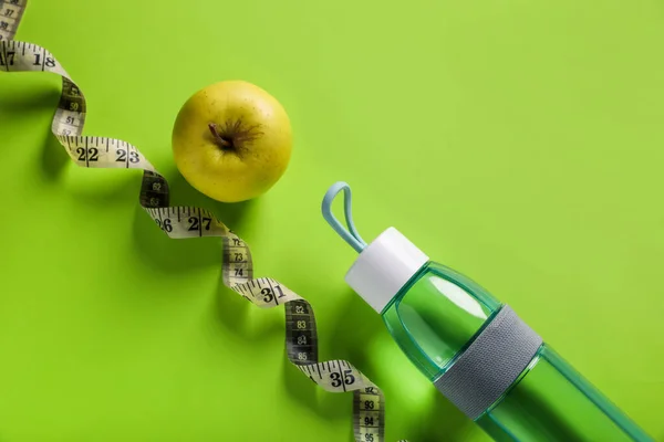 Measuring tape, bottle with water and apple on light green background, flat lay. Weight control concept