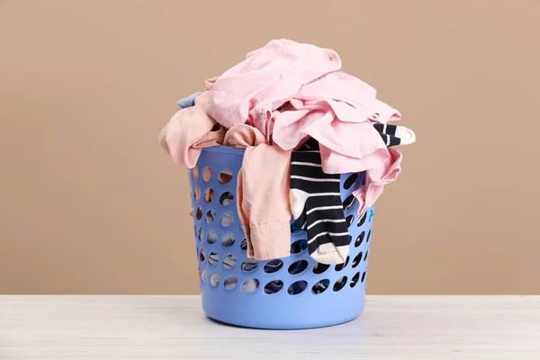 Plastic laundry basket with clothes near beige wall