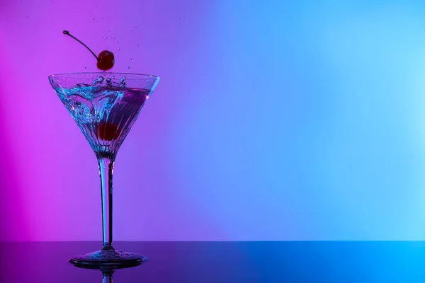 Adding cherries into glass with martini on table in neon lights, space for text