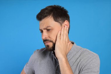 Açık mavi arka planda kulak ağrısı çeken bir adam.