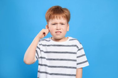 Little boy suffering from ear pain on light blue background