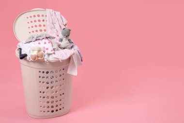 Laundry basket with baby clothes and soft toy on light pink background. Space for text